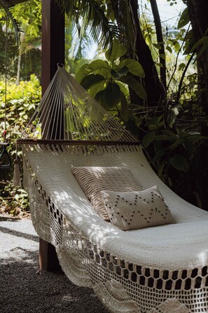 A hammock bed with a woven canopy, a single pillow, and a natural outdoor setting with trees and plants.