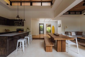 Una cocina moderna con una isla de madera, taburetes de bar blancos y un comedor con mesa de madera y sillas blancas.