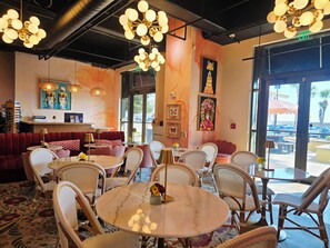 A modern interior with round tables and wicker chairs, a red sofa, and artwork on the walls.