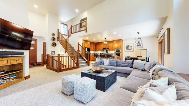 A spacious living room with a large sectional sofa, a flat-screen TV, a staircase, and a kitchen area. - Pet-Friendly, Bright, Updated & On Golf Course! Private Game Room and Hot Tub (Mammoth Lakes)