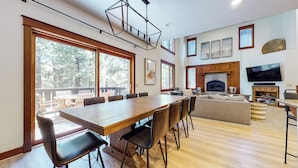 A spacious living area with a large wooden dining table, comfortable seating, a fireplace, and a television mounted on the wall. - Pet-Friendly, Bright, Updated & On Golf Course! Private Game Room and Hot Tub (Mammoth Lakes)