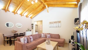 A modern living room with a wooden ceiling, a pink sofa, a wooden coffee table, a dining table with chairs, and a TV stand. - Villa Bella Luna (Zakynthos)