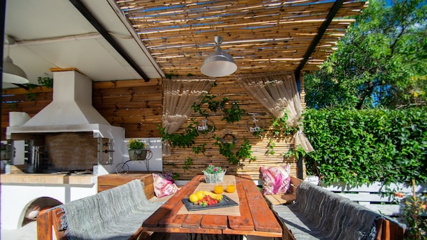 An outdoor dining area with a wooden table and benches, surrounded by greenery and a pergola. - Villa Bella Luna (Zakynthos)