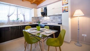 A modern kitchen with a dining table set for four, green chairs, and a large window with curtains. - Villa Bella Luna (Zakynthos)
