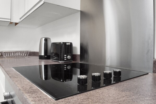 A modern kitchen with a black induction cooktop, stainless steel appliances, and a granite countertop. - Blackie's Neuk Ideal For Uni / West End (Dundee)