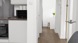 A modern kitchen with white cabinets, a microwave, and a stainless steel range hood. A wooden floor leads to a dining area with a table and chairs.