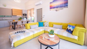 Uma sala de estar moderna com um sofá amarelo, uma área de refeições com cadeiras e uma cozinha ao fundo.