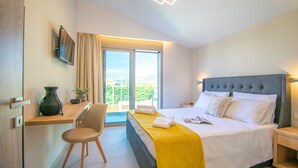 Quarto de hotel moderno com cama, escrivaninha, cadeira e uma grande janela com vista para o exterior.