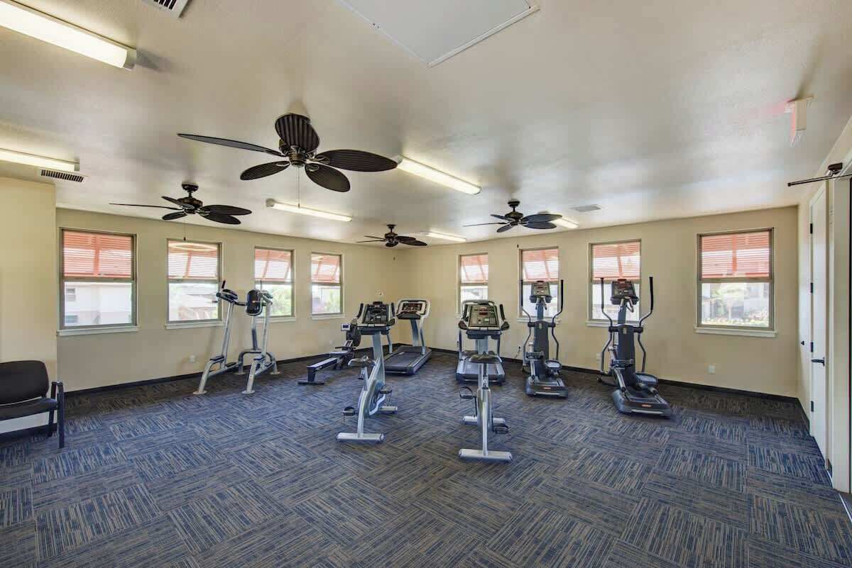 Une salle de sport équipée de tapis de course, de vélos elliptiques et de vélos d’appartement, et dotée de ventilateurs au plafond et de grandes fenêtres.