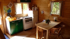 Cocina compacta con paredes de madera, un mueble verde, una estufa blanca y una mesa de comedor con sillas de mimbre.