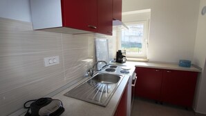 A compact kitchen with red cabinets, a stainless steel sink, and a window providing natural light. - Modern apartment Tomislav 1 on the island of Krk (Malinska)