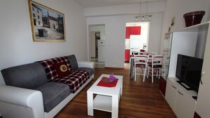 A modern living room with a grey sofa, a small white table, and a TV. A red and black checkered blanket is draped over the sofa. The room has wooden flooring and white walls. - Modern apartment Tomislav 1 on the island of Krk (Malinska)