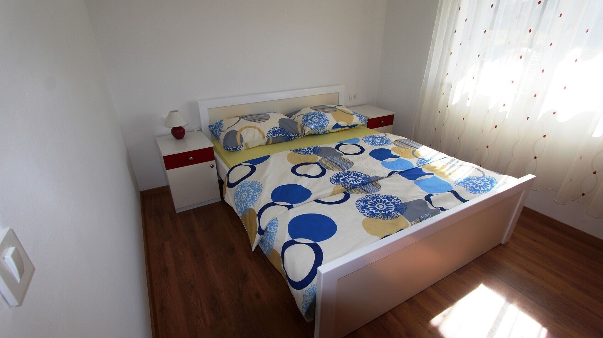A bedroom with a bed, nightstand, lamp, and curtains.