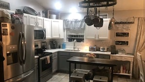 A compact kitchen with a refrigerator, microwave, stove, and hanging pots. - Hometown Haven in Glens Falls, NY (between Lake George & Saratoga) (Glens Falls)