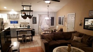 A living room with a brown sofa, a glass coffee table, and a dining area with a table and chairs. - Hometown Haven in Glens Falls, NY (between Lake George & Saratoga) (Glens Falls)