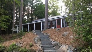 Een chalet met een stenen trap die leidt naar een veranda, omringd door bomen en een waterpartij.