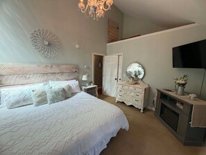 A bedroom with a large bed, a dresser, a television, and a chandelier. - Waterfront Hudson River Retreat, Near Lake George & Saratoga, Hot tub, Dock (corinth)