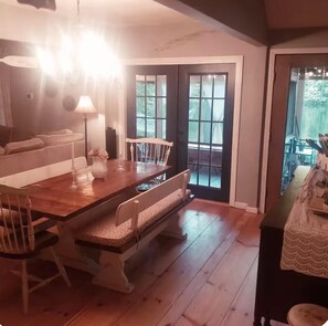 A dining area with a wooden table, chairs, and a bench. There is a lamp on the table, and a door leading outside. - Waterfront Hudson River Retreat, Near Lake George & Saratoga, Hot tub, Dock (corinth)