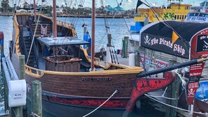 Un bateau en bois, baptisé « Royal Conquest », était amarré dans une marina, sous un ciel dégagé et avec un paysage tropical en toile de fond.