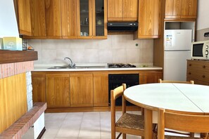 A kitchen with wooden cabinets, a gas stove, a sink, a microwave, and a dining table with chairs. - S228 - Sirolo, three-room apartment near the center (Sirolo)