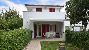 A two-story white building with a covered patio, red shutters, and a small garden area with a table and chairs. - M272 - Marcelli, new three-room apartment with garden (Marcelli)