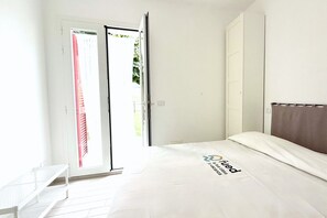 A hotel room with a bed, a white bench, and a sliding glass door leading to a balcony.