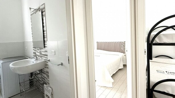 A hotel room with a white sink, mirror, and bed with white bedding. - M272 - Marcelli, new three-room apartment with garden (Marcelli)