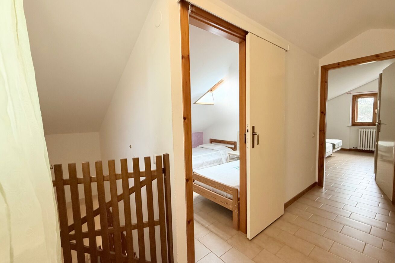 Habitació amb un llit, una porta de fusta i una obertura cap a una altra estada.