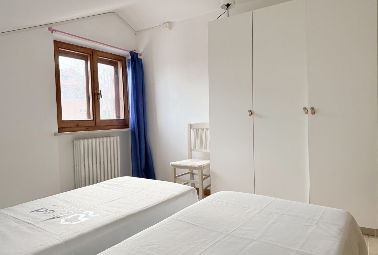 Une chambre avec deux lits, une fenêtre avec des rideaux, un radiateur, une chaise et une armoire.