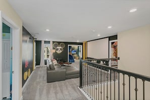 Un couloir avec un canapé gris, un escalier doté d’une rampe noire et un mur orné d’une fresque représentant Mickey Mouse.