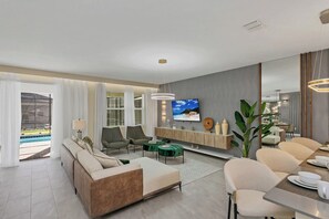 Un salon moderne comprenant un canapé, des fauteuils, un téléviseur et un coin repas.