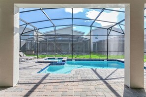 Une piscine extérieure couverte, protégée par une structure en verre, entourée d’une terrasse dallée.