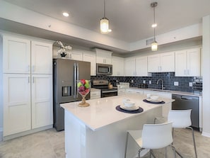A modern kitchen with white cabinetry, stainless steel appliances, and a central island with seating.