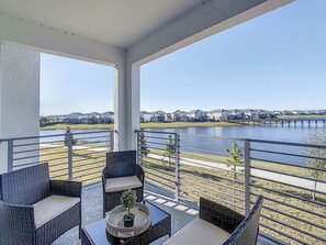 A balcony with wicker furniture and a view of a lake and buildings.
