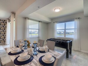 A dining area with a table set for four, a foosball table, and large windows with a view.
