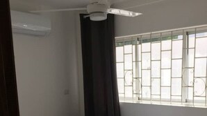 Een slaapkamer met een enkel bed, een plafondventilator, een raam met metalen tralies en uitzicht op buiten.