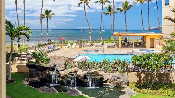 A resort pool area with palm trees, a waterfall, and a view of the ocean.