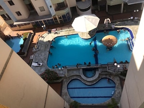An indoor swimming pool with multiple lanes, a central water slide, and a surrounding deck area with seating and umbrellas.