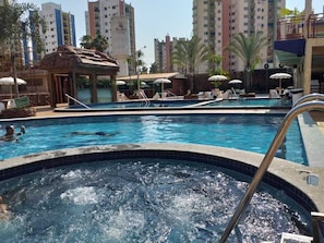 A swimming pool with a hot tub, lounge chairs, and umbrellas.