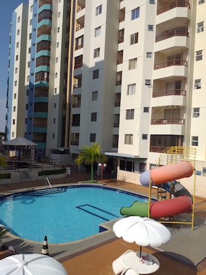 A swimming pool with a slide, surrounded by a multi-story building with balconies.