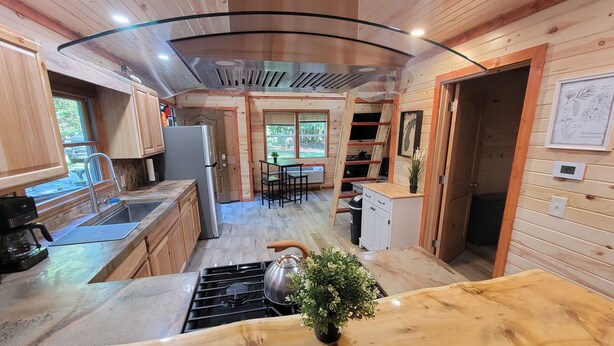 Eine moderne Küche mit Holzschränken, einem Edelstahlkühlschrank, einem Gasherd und einer Spüle. Ein Essbereich mit Tisch und Stühlen bietet einen Blick ins Freie.