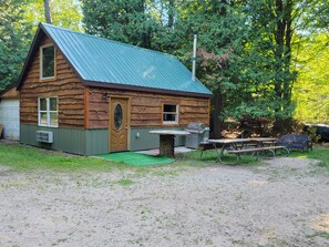 Une cabane rustique avec un toit en métal vert, une porte en bois et un petit porche.