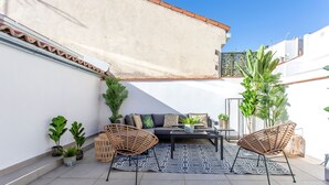 A patio with two wicker chairs, a sofa, and a coffee table. There are potted plants and a patterned rug. - Genteel Home Madrazo IV Terrace (Madrid)