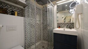 A modern bathroom with a glass-enclosed shower, a white sink with a mirror, and a tiled floor. - C3D Greenery (París)