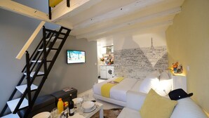 A compact living space with a sofa, a dining table with plates and glasses, a TV, a washing machine, and a map of Paris on the wall. - C3D Greenery (París)