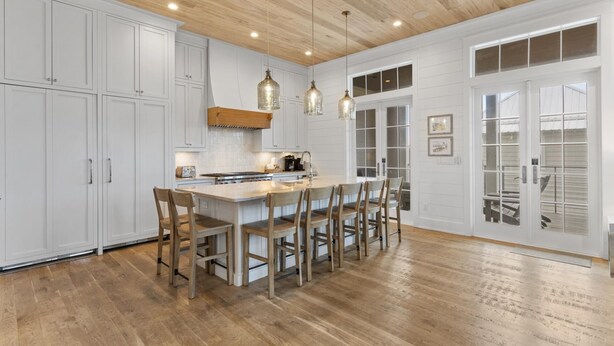 Une cuisine avec des meubles blancs, un plafond en bois et des luminaires suspendus.