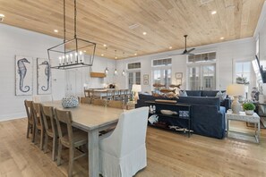 A spacious living area with a wooden ceiling, a dining table with chairs, a sofa, and a coffee table.