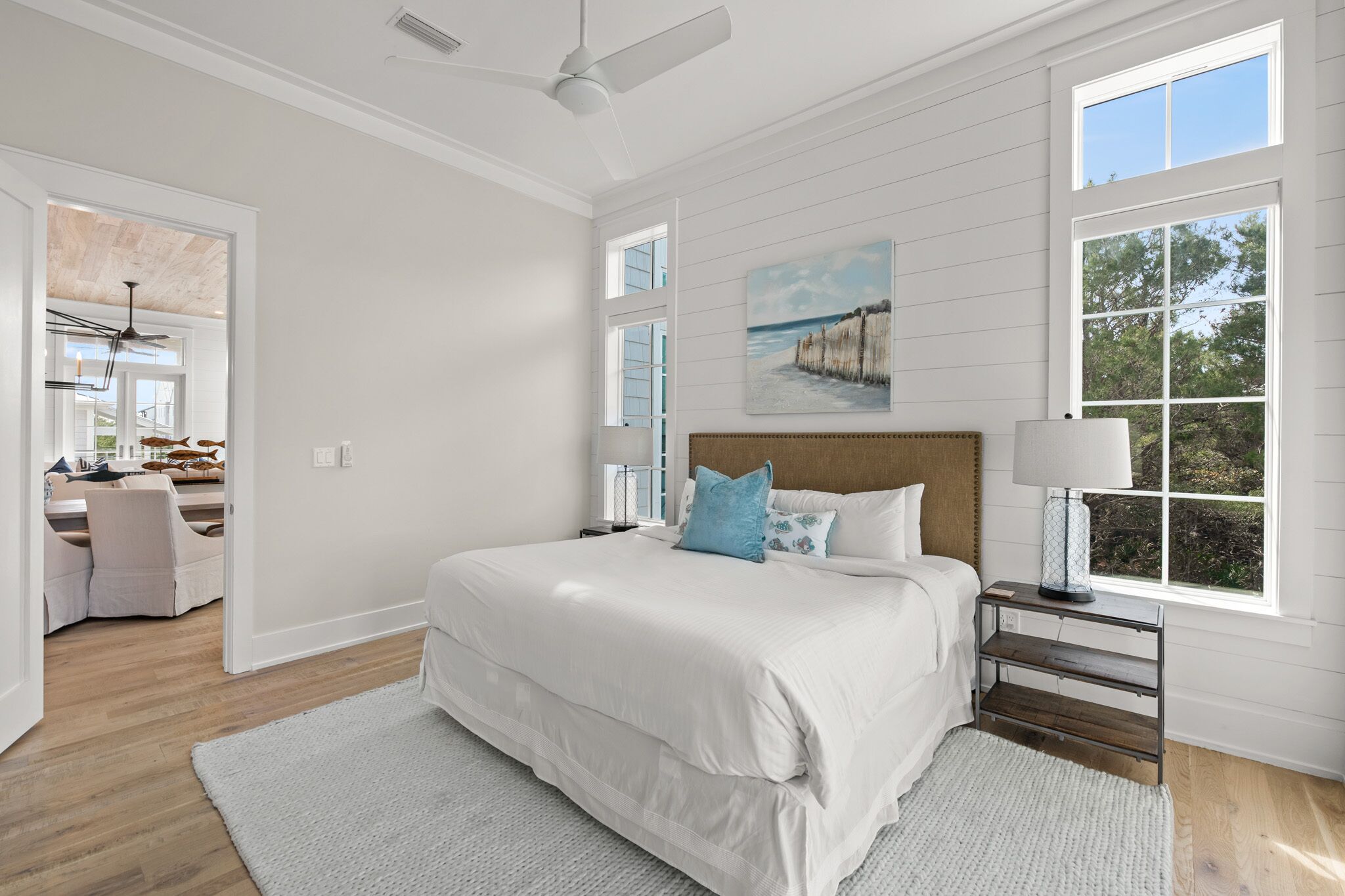 A bedroom with a large bed, a headboard, a nightstand, a lamp, and a window with a view of trees.