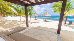 A beach view with thatched umbrellas, lounge chairs, and palm trees.