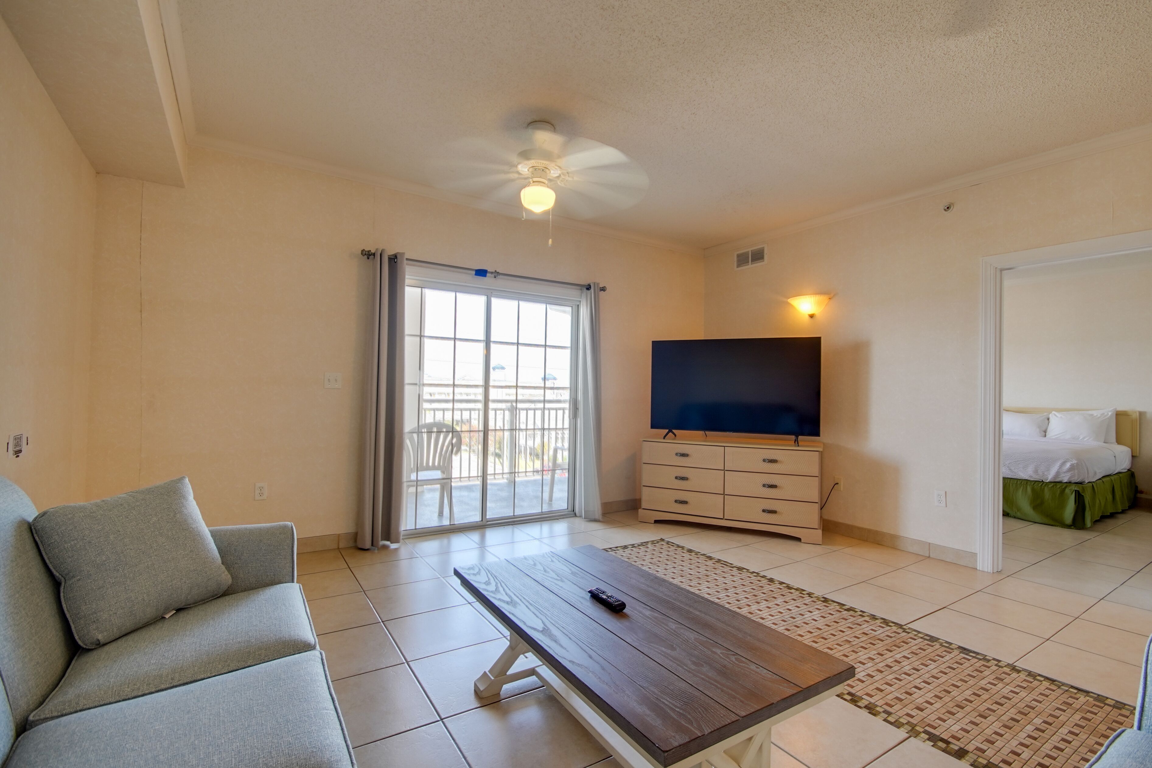 A living room with a sofa, a coffee table, a TV, and a sliding glass door leading to an outdoor area.